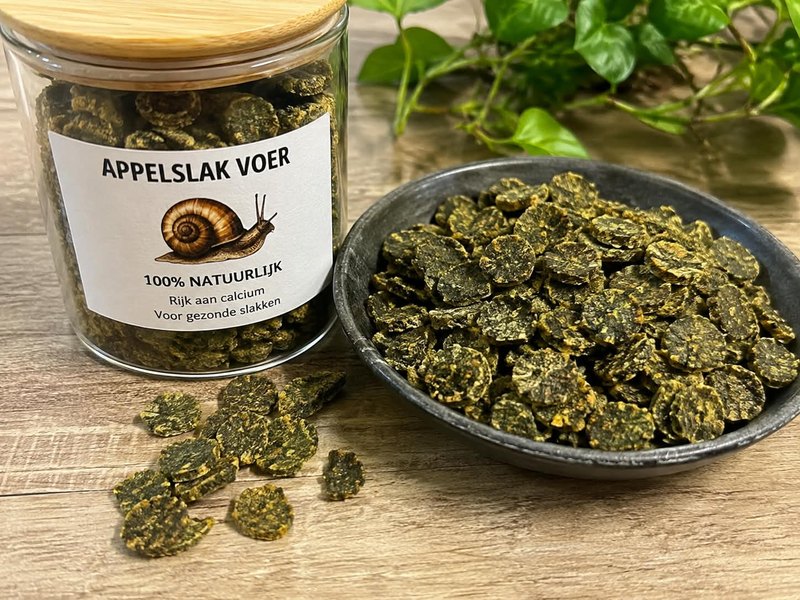 Pot appelslakkenvoer van AquaSlak naast een schaaltje groene voerschijfjes